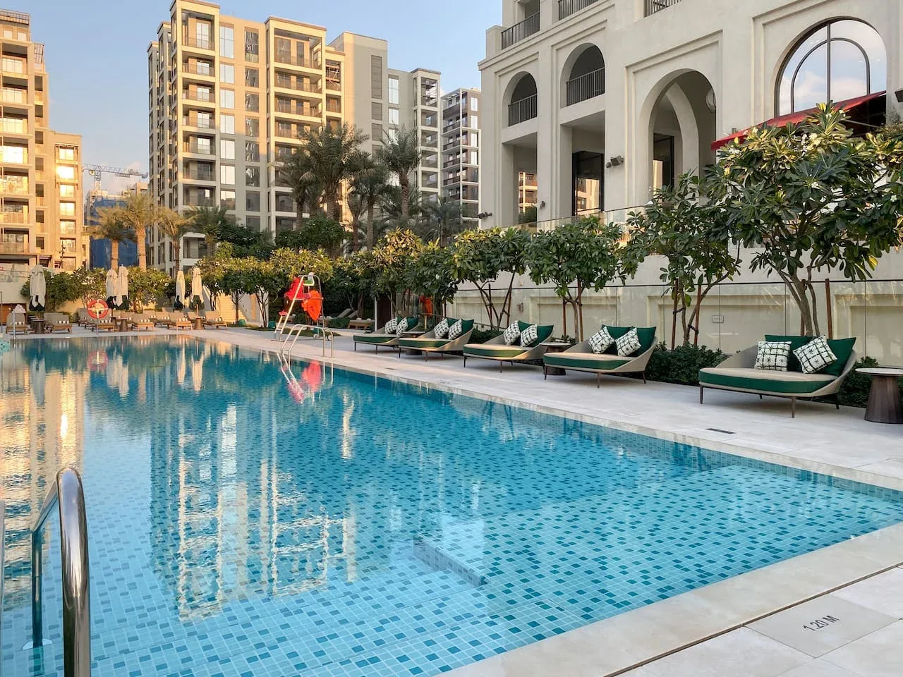 Una piscina junto a una zona ajardinada con asientos y edificios altos.