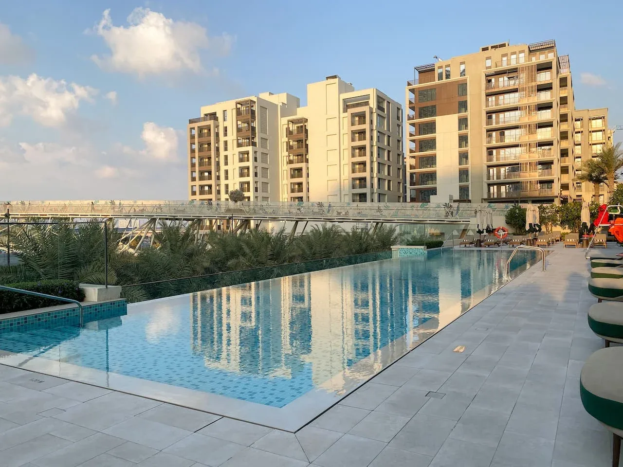 Una piscina junto a una terraza pavimentada, con edificios de apartamentos al fondo.