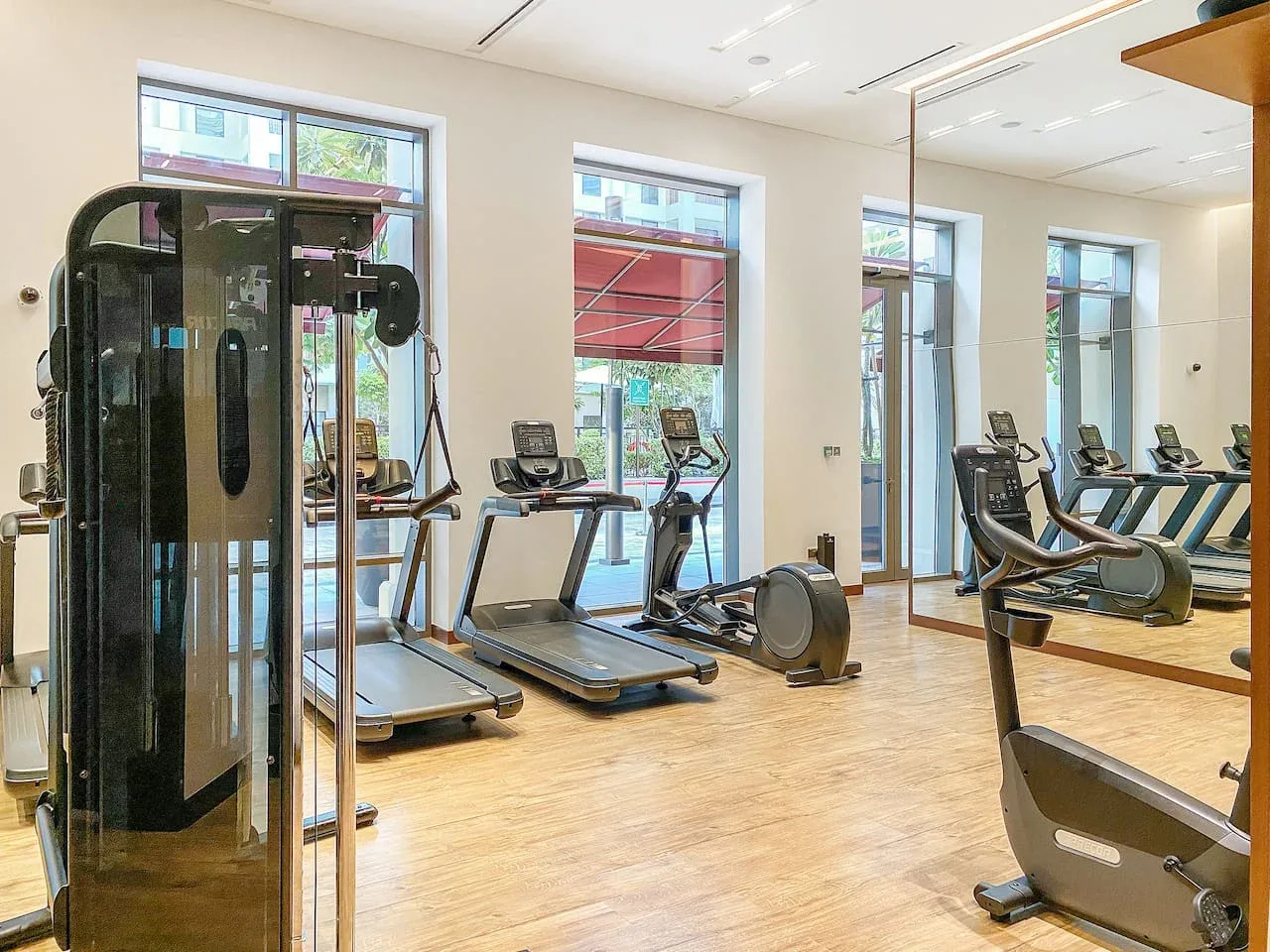 Una sala de ejercicio luminosa con cintas de correr y otros equipos junto a grandes ventanas.