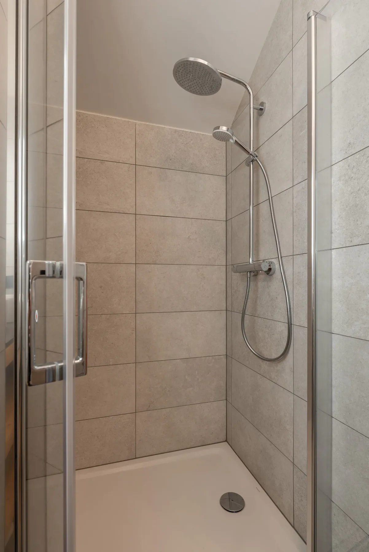 Modern bathroom with double sinks, a large illuminated mirror, wooden shelving, and a glass-enclosed walk-in shower.