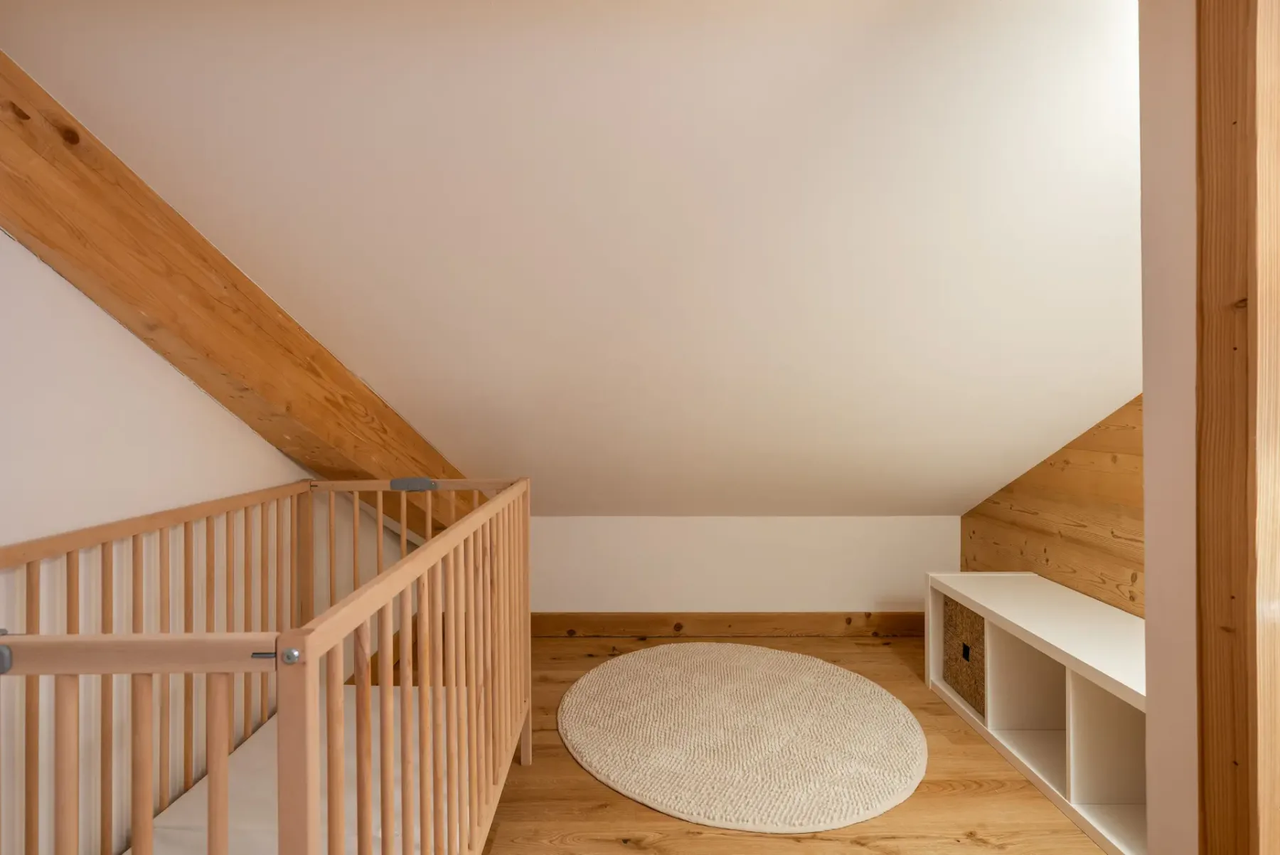 A cozy ensuite bedroom with wood-paneled walls, a double bed with grey and plaid bedding, bedside tables, a mirror, and a balcony door letting in natural light.