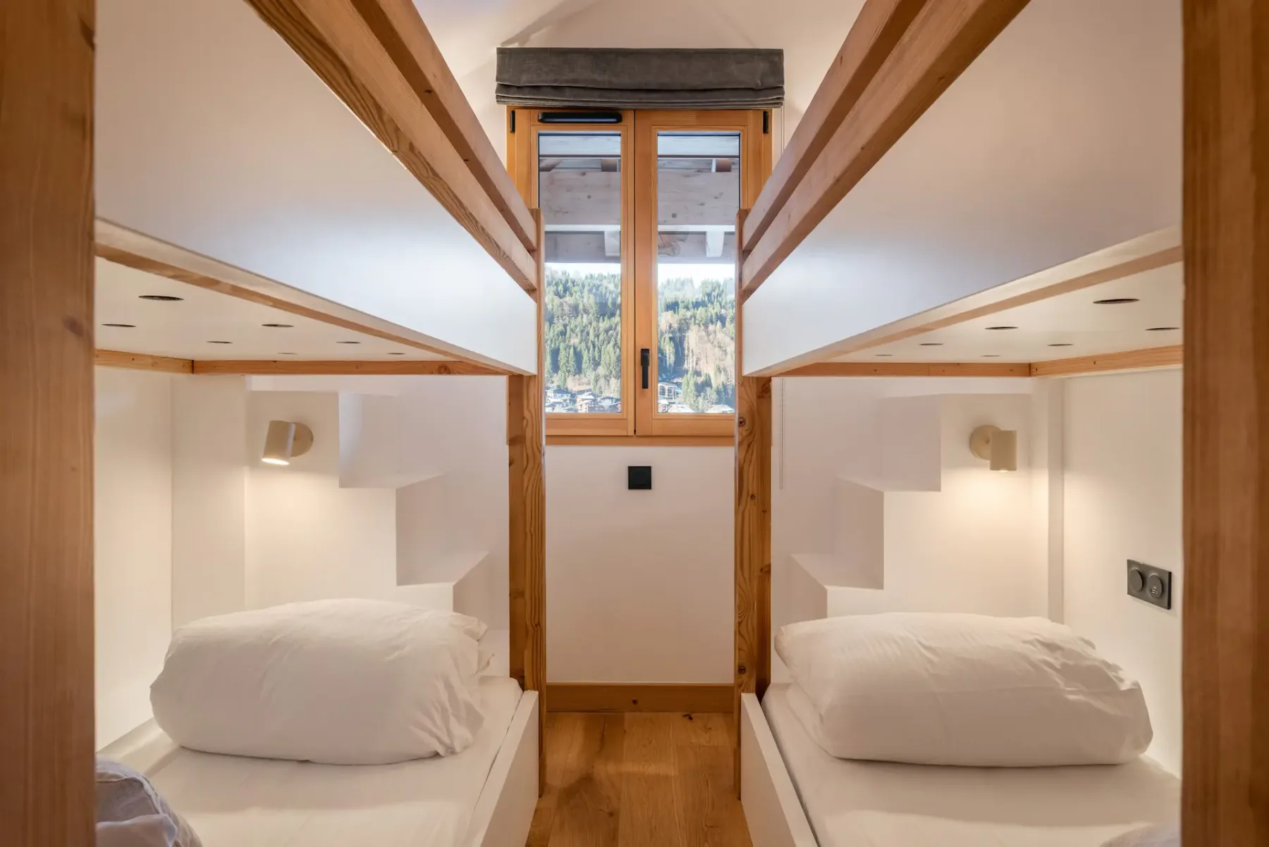 A cozy bedroom with two wooden bunk beds, white bedding, a round furry bean bag chair, a small wooden stool, and warm ambient lighting.