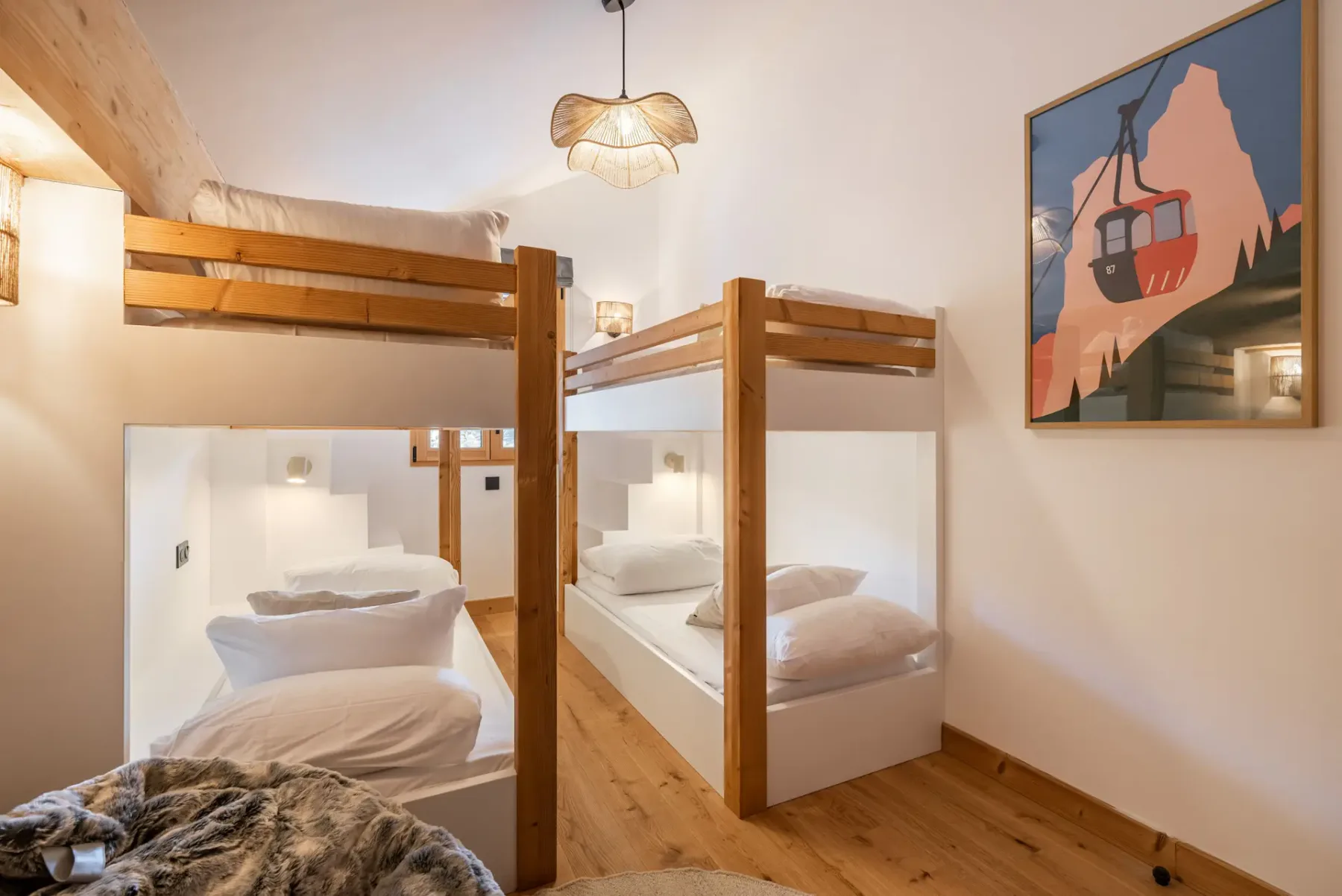 A cozy bedroom with two wooden bunk beds, white bedding, a round furry bean bag chair, a small wooden stool, and warm ambient lighting.