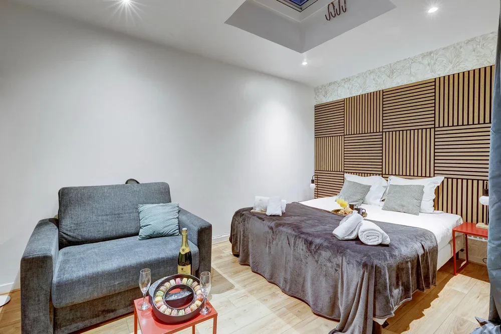 A bedroom with a bed, gray seating, and a patterned wood accent wall.