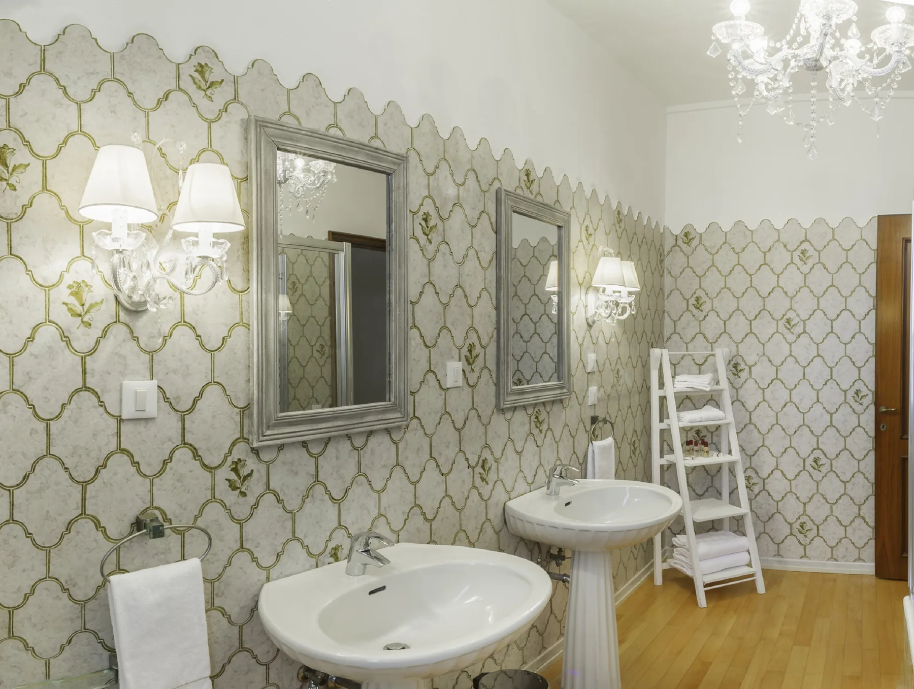 A bathroom with pedestal sinks, decorative patterned walls, and a white ladder-style rack.