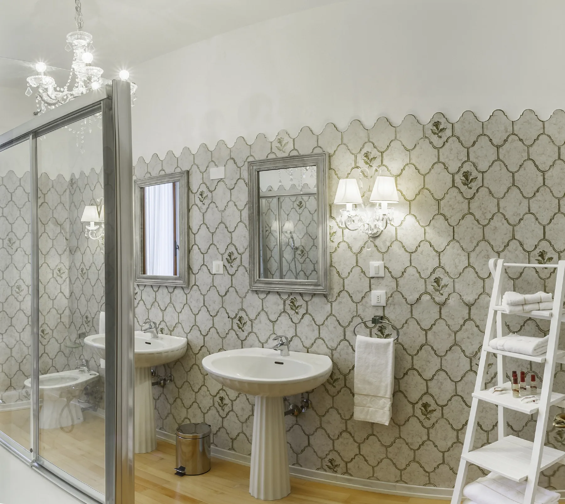 A bathroom with a pedestal sink, patterned walls, and a glass shower enclosure.