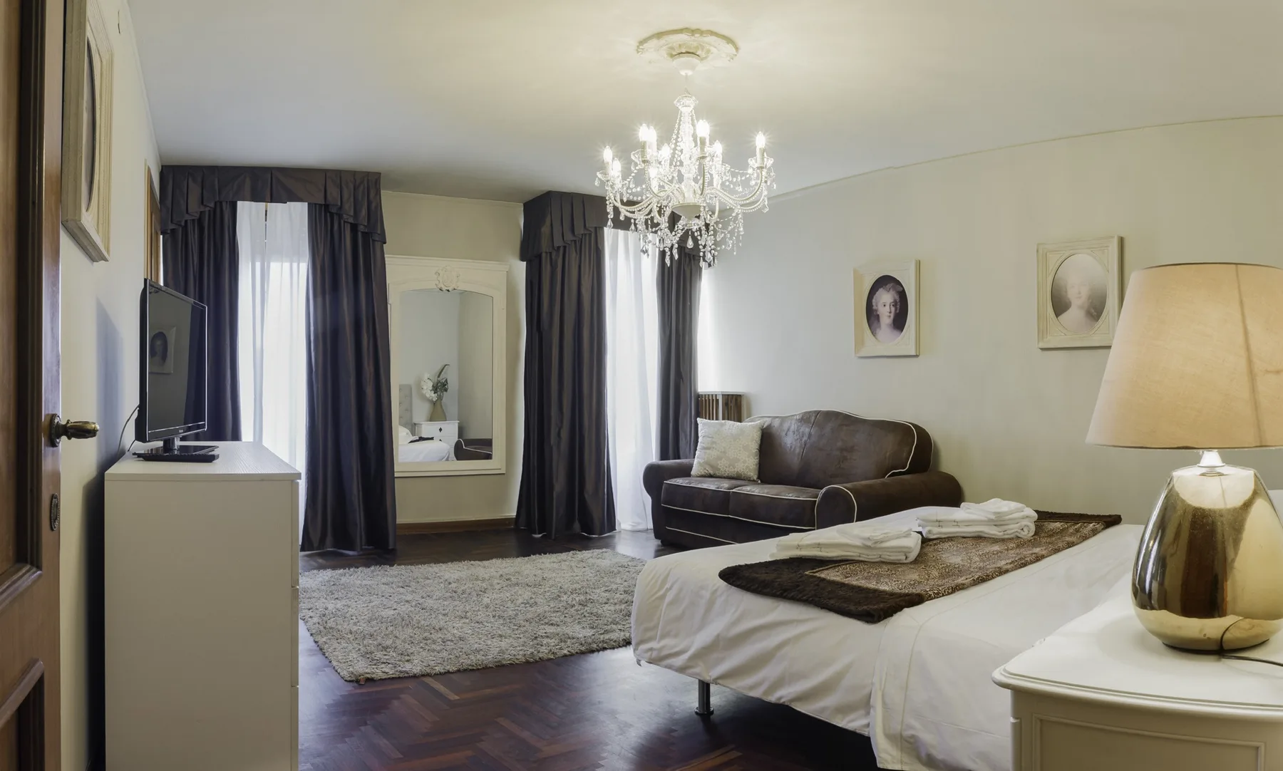 A bedroom with a bed, seating area, and chandelier.