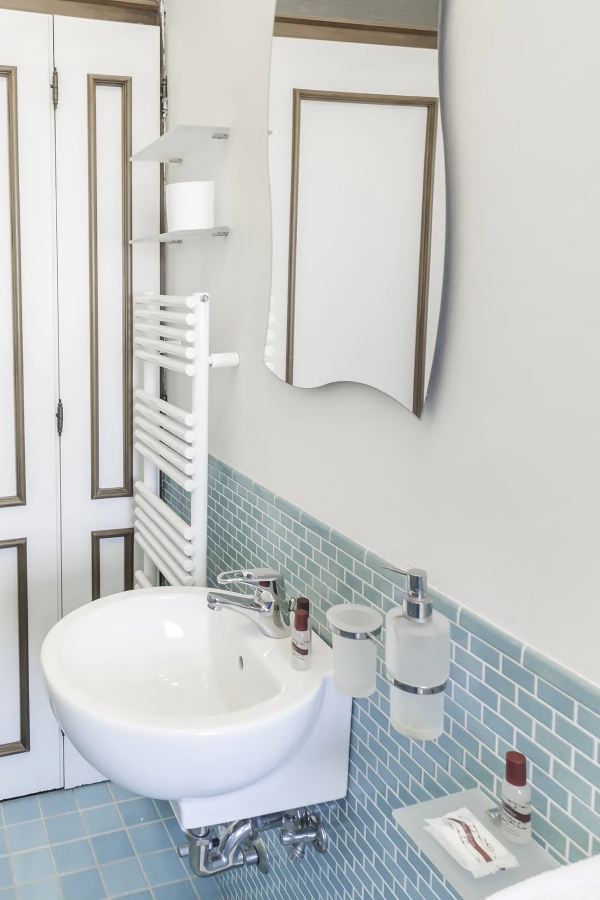 A bathroom sink beneath a mirror, with blue tile along the wall.