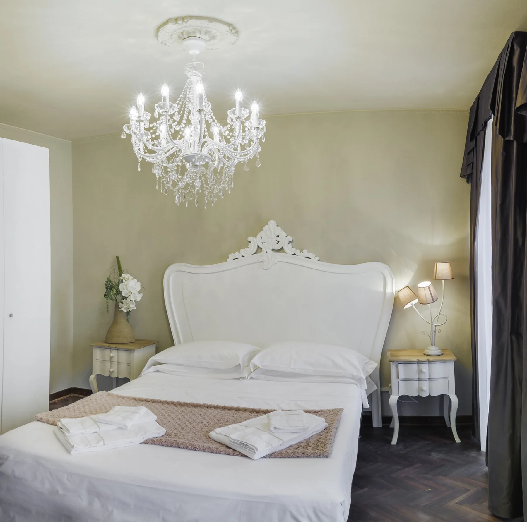 A bedroom with a large bed, bedside tables, and a chandelier.