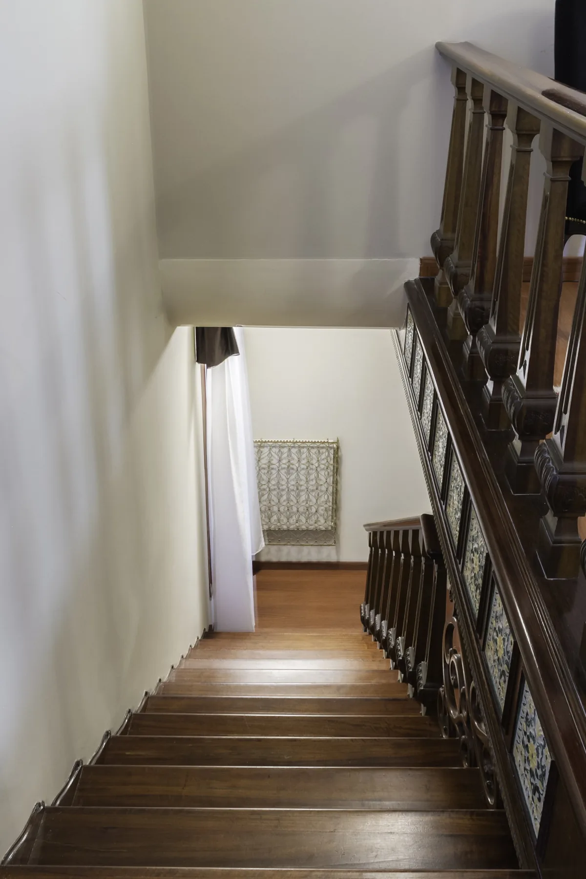 A wooden staircase descends beside a patterned tiled railing.