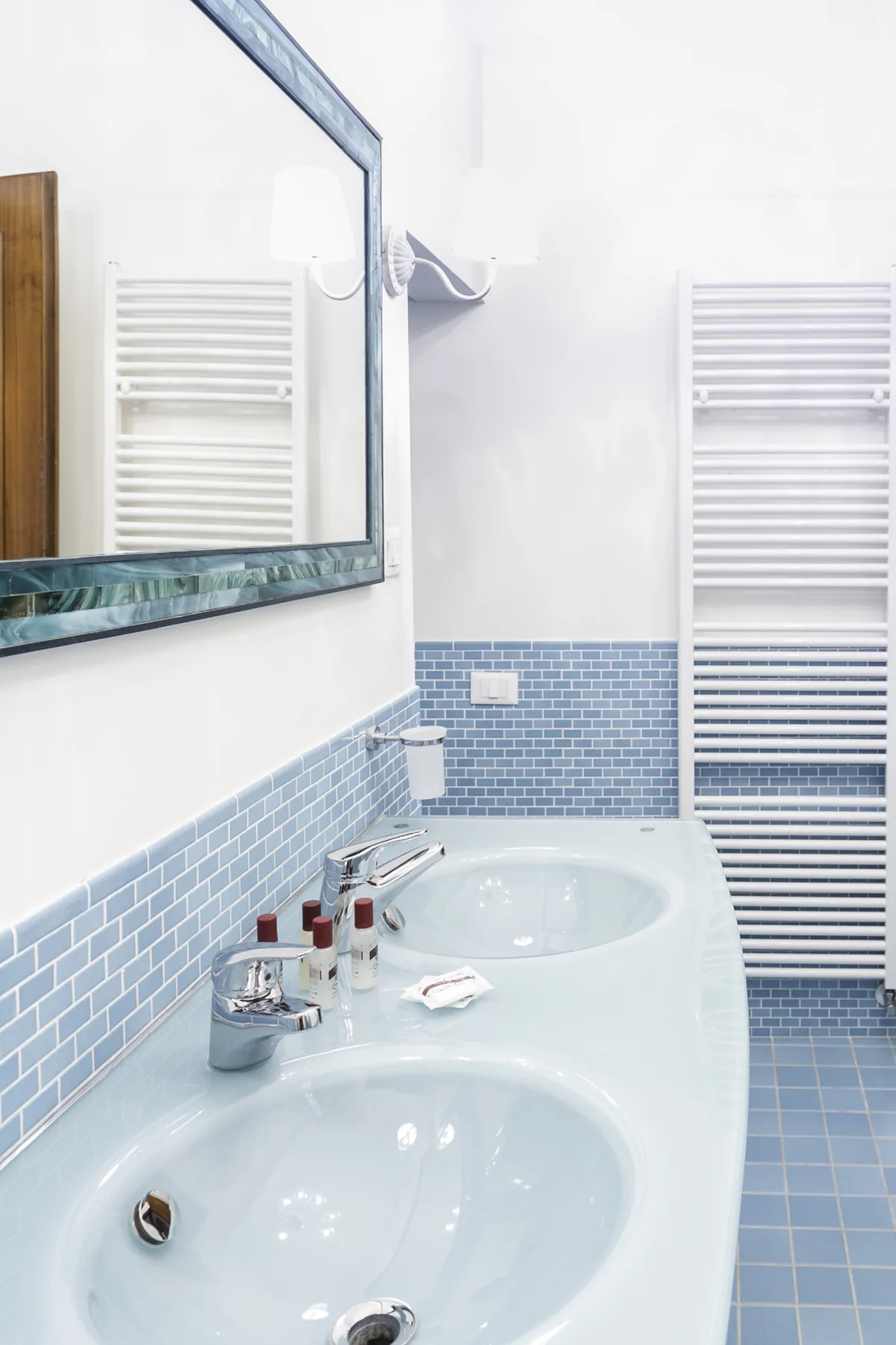 A bathroom with a double sink vanity, blue tile, and wall-mounted towel warmers.
