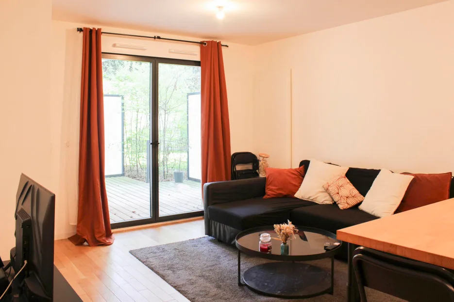 Una sala de estar con asientos oscuros junto a puertas de vidrio y cortinas naranjas.