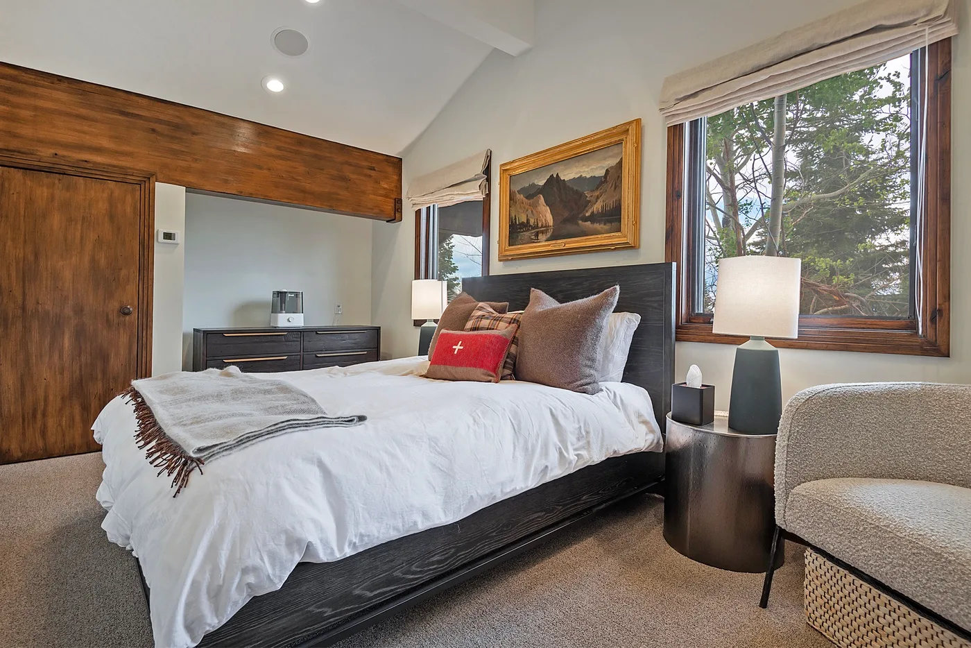 A bedroom with a neatly made bed beside a large window overlooking trees.