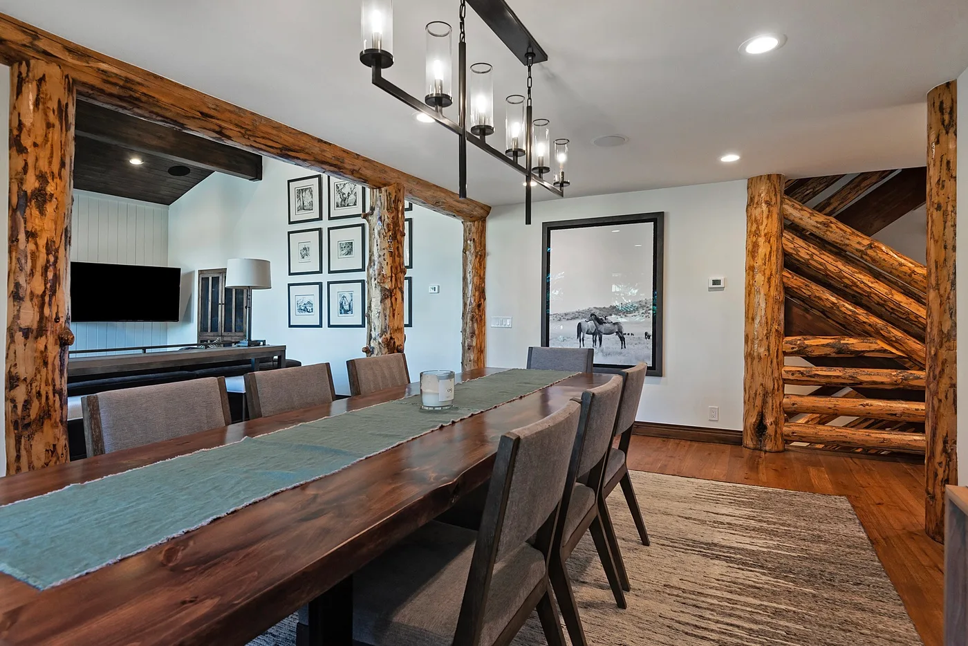 A dining area features a long wooden table and chairs beneath a hanging light.