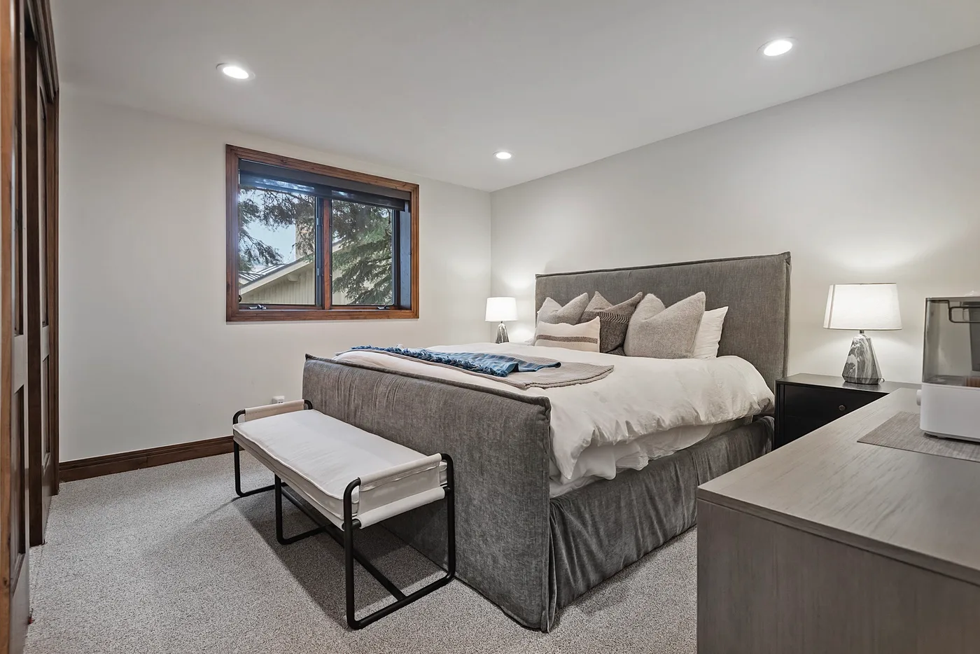 A bedroom with a large bed, a window, and a bench at the foot.