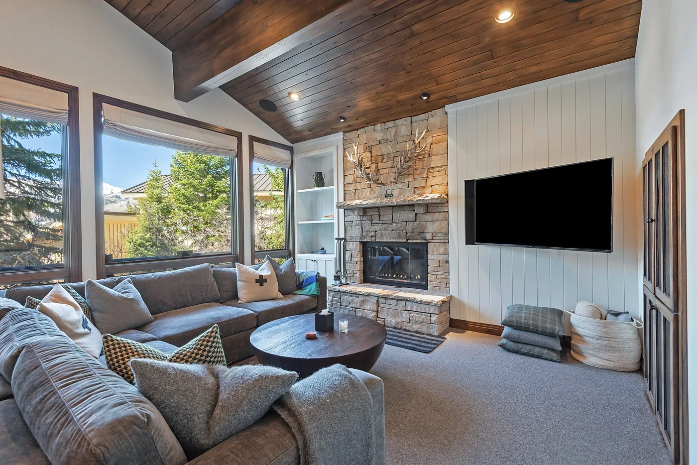A living room with sectional seating, a stone fireplace, and a wall-mounted television.