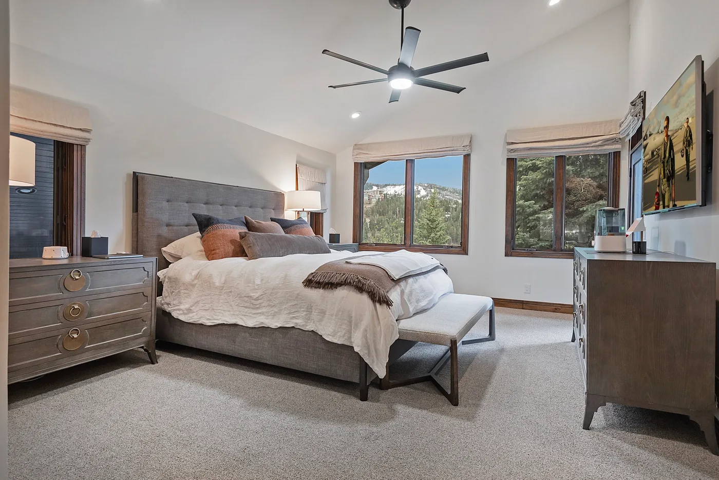 A bright bedroom with a bed, large windows, and a ceiling fan.