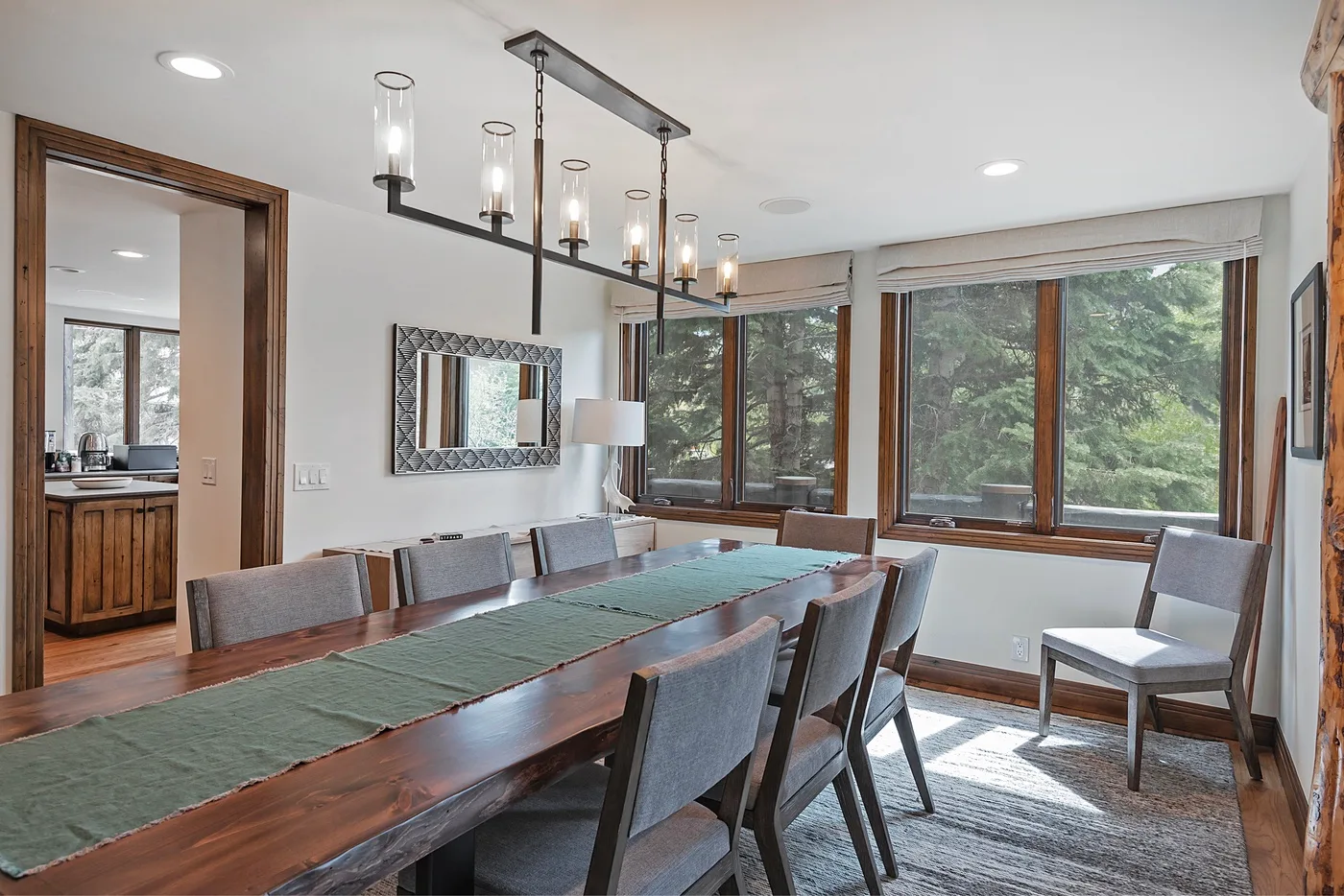 A dining area with a long wooden table and large windows overlooking trees.