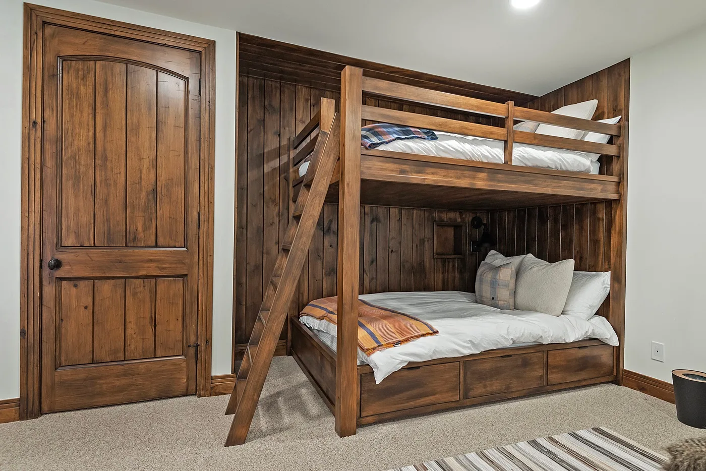 A bedroom with a wooden bunk bed, white bedding, and a wooden door.