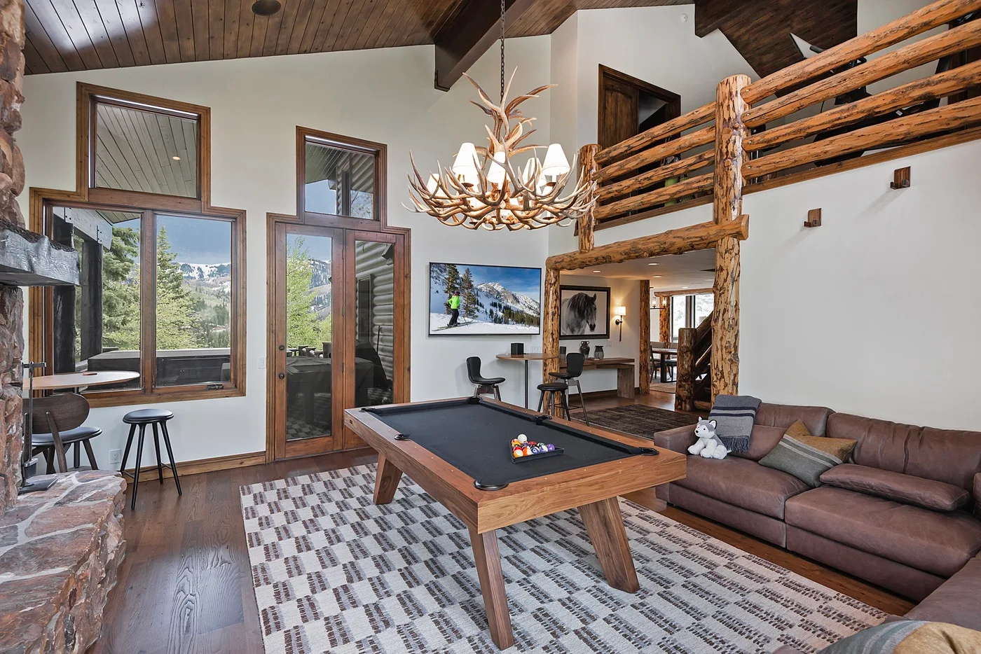 A double-height game room features a pool table and an open wooden loft railing.