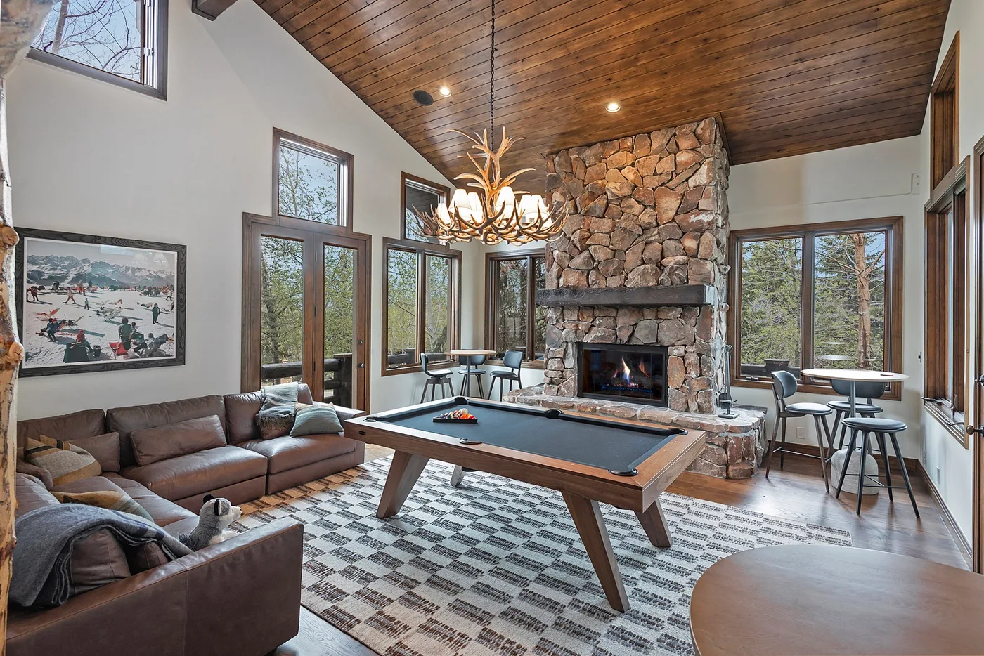 A living room with a pool table, seating, and a stone fireplace.