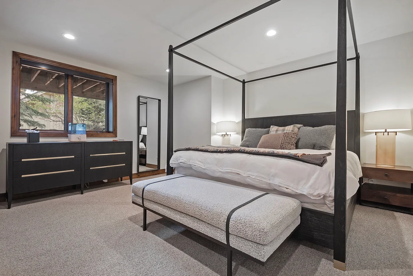 A bedroom with a four-poster bed, a bench, and a dresser beside the window.
