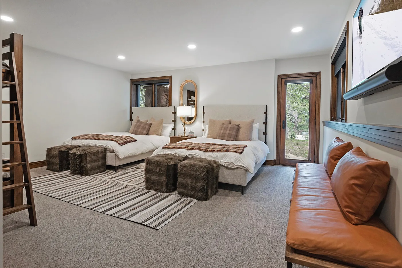A bedroom with two beds, striped rugs, and a leather bench.