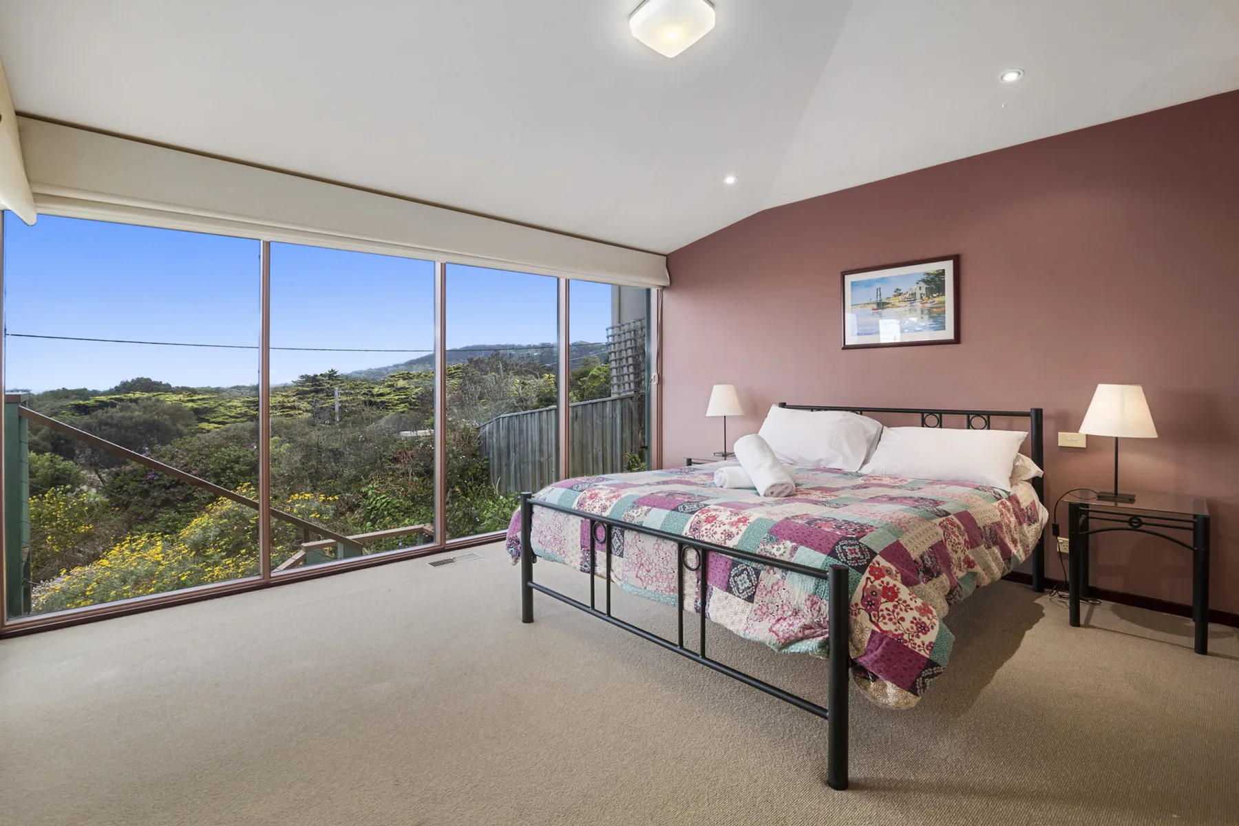 Un dormitorio con una cama de metal y grandes ventanales con vistas a un paisaje verde.
