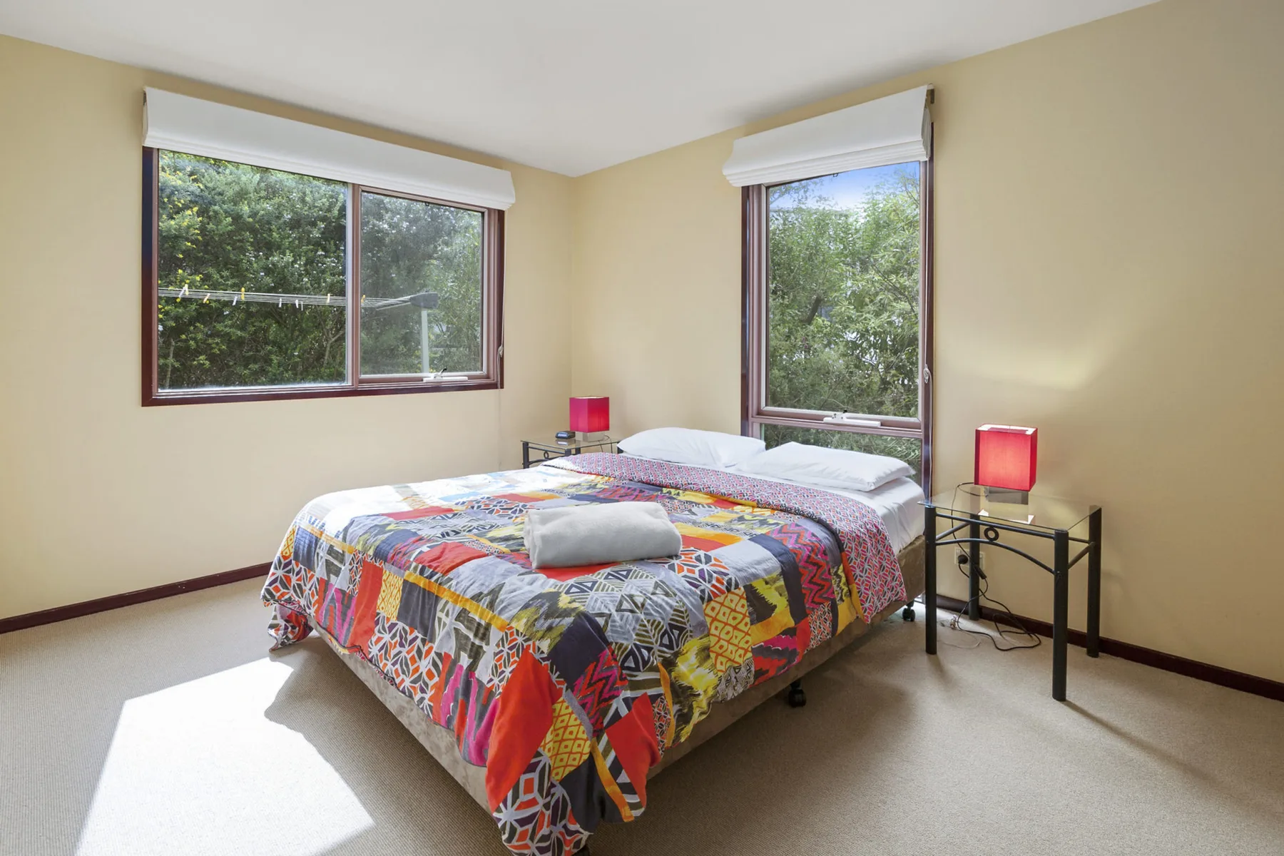 Un dormitorio con una colcha colorida y ventanas con vistas a la vegetación.