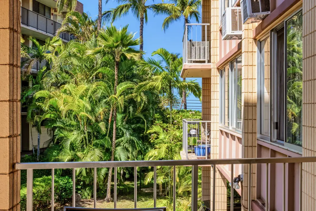 A balcony overlooks lush tropical greenery and neighboring apartment buildings.