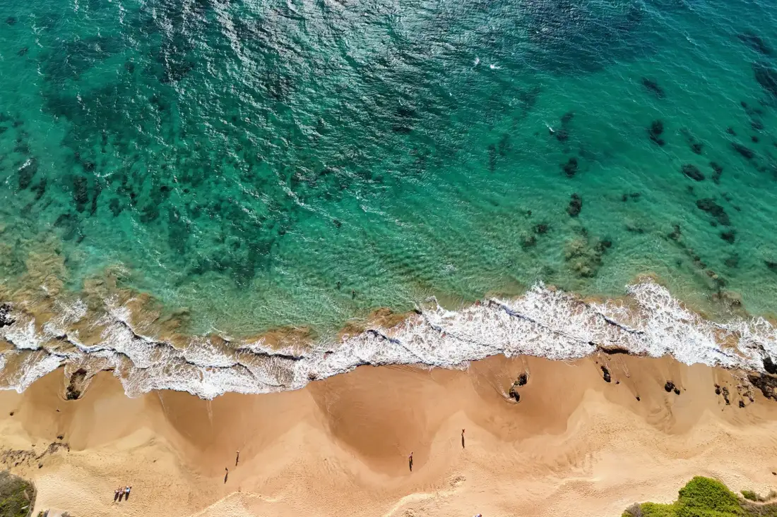 An aerial view of turquoise water meeting a sandy beach.