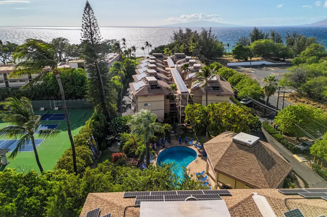 An aerial view of a resort complex with a pool, tennis court, and ocean beyond.