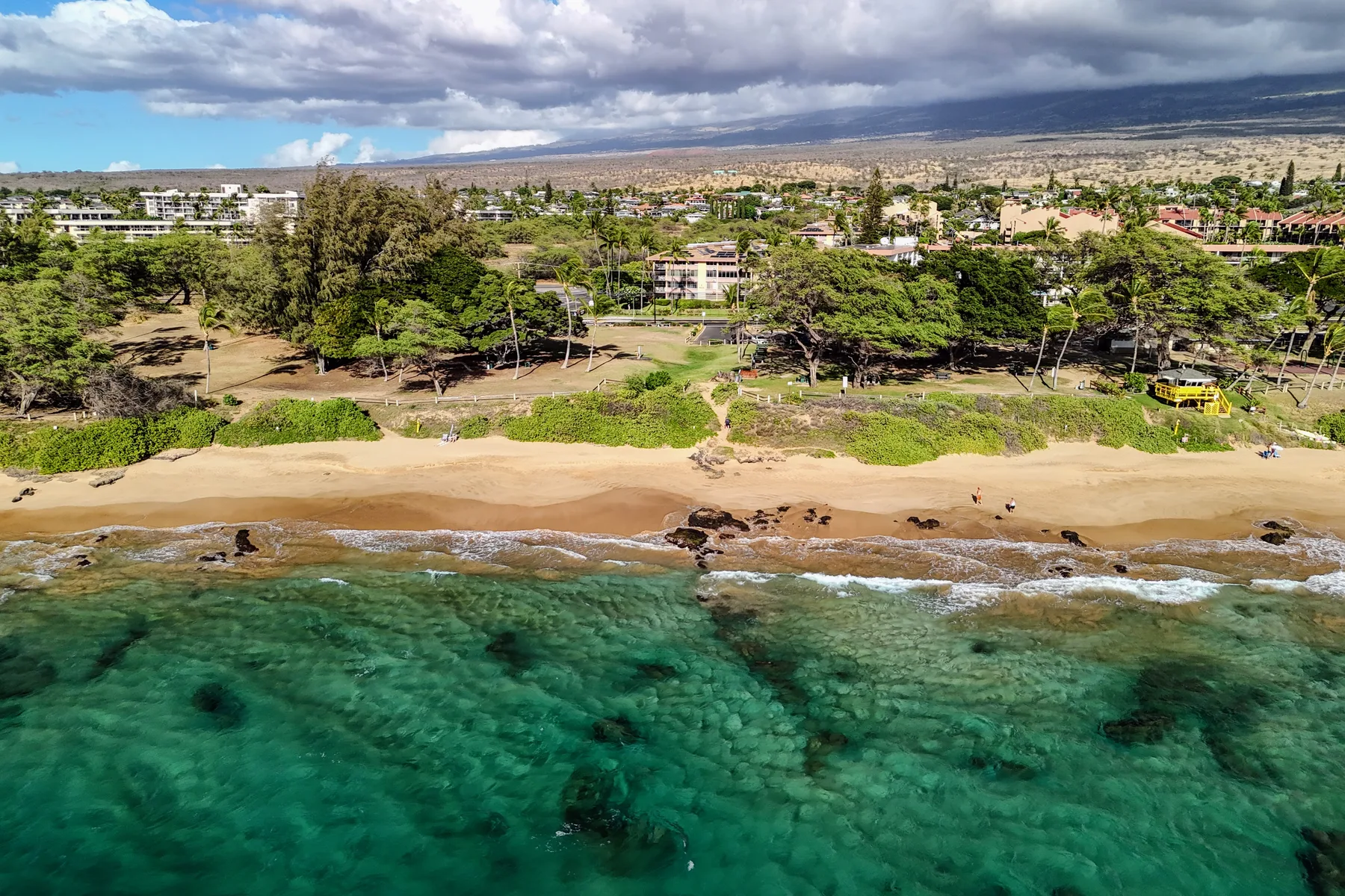 Aerial view of a sandy beach with clear turquoise water and trees along the shore.
