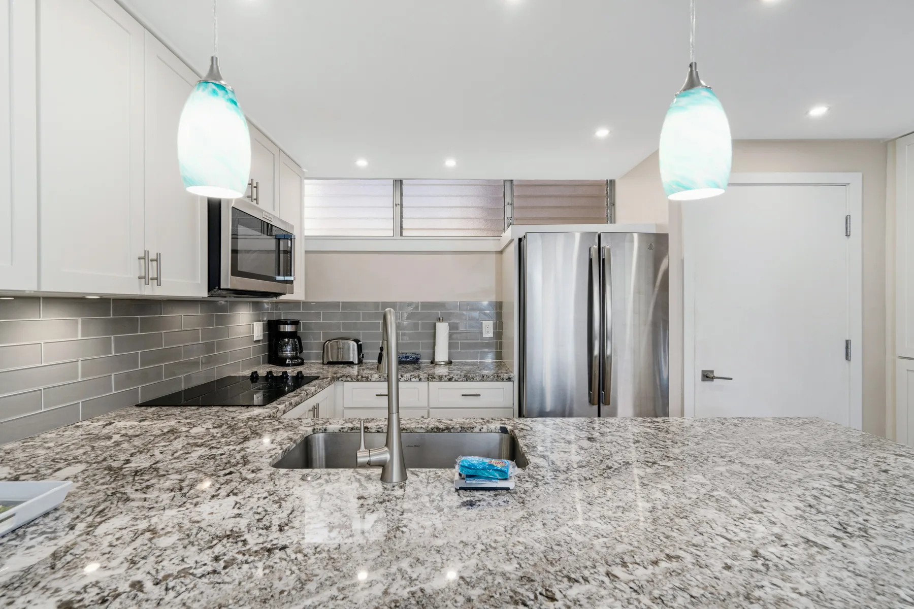 A bright kitchen with a large stone-patterned island and stainless steel appliances.