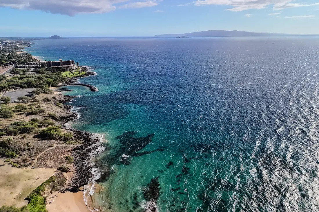Aerial coastal view of clear blue water beside a rocky shoreline.