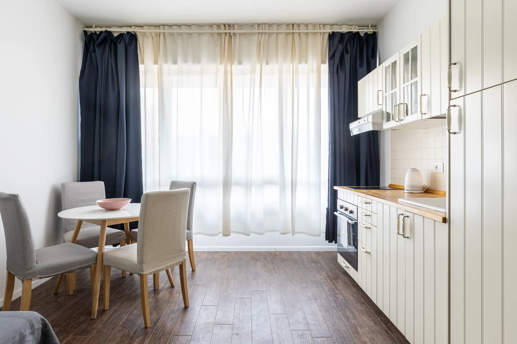 Un comedor luminoso junto a una cocina, con una mesa y armarios.