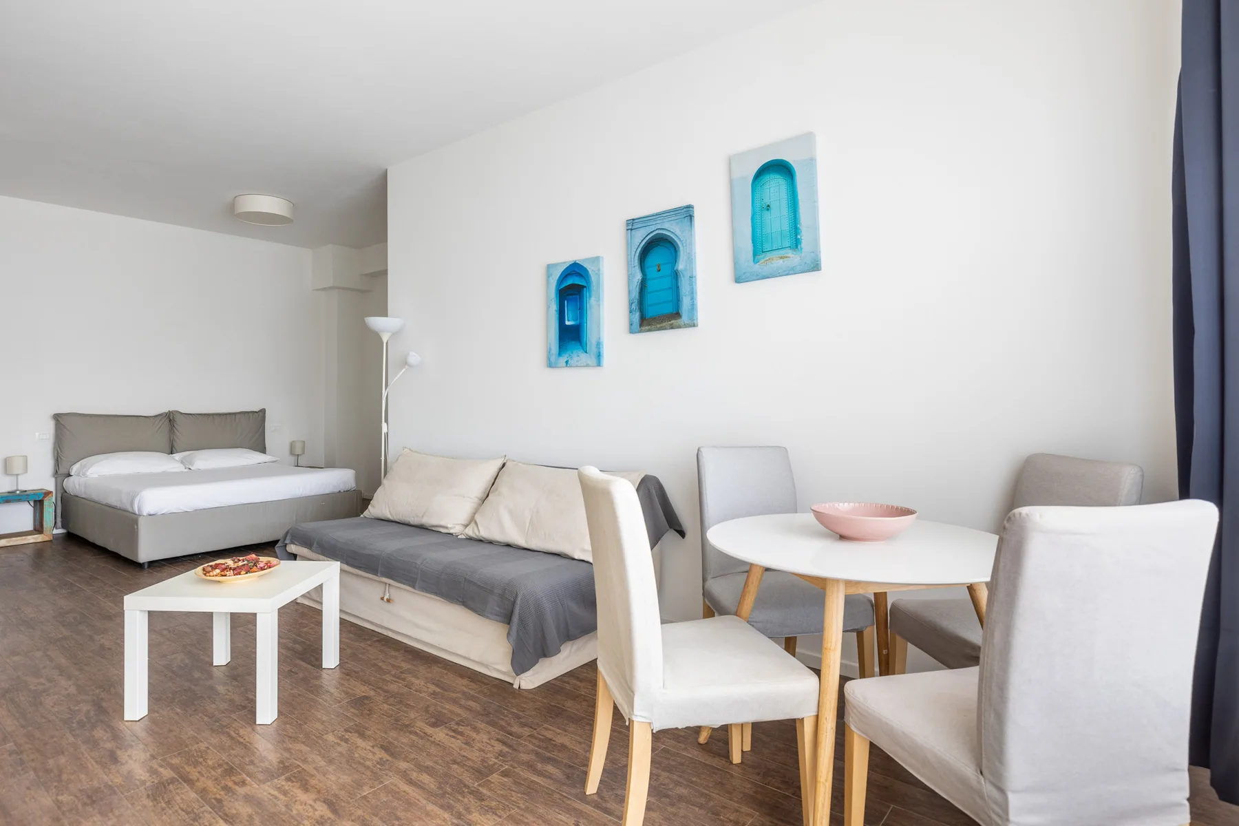 Un dormitorio luminoso con zona de estar, cama, sofá y mesa de comedor.
