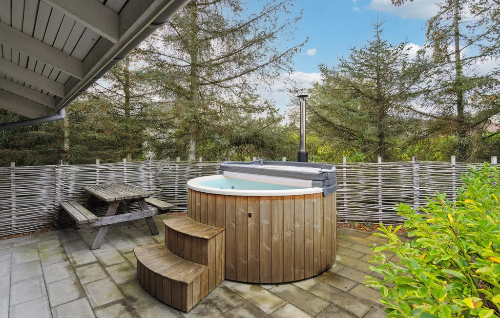 Una bañera de hidromasaje exterior está en un patio pavimentado junto a una mesa de picnic y árboles.