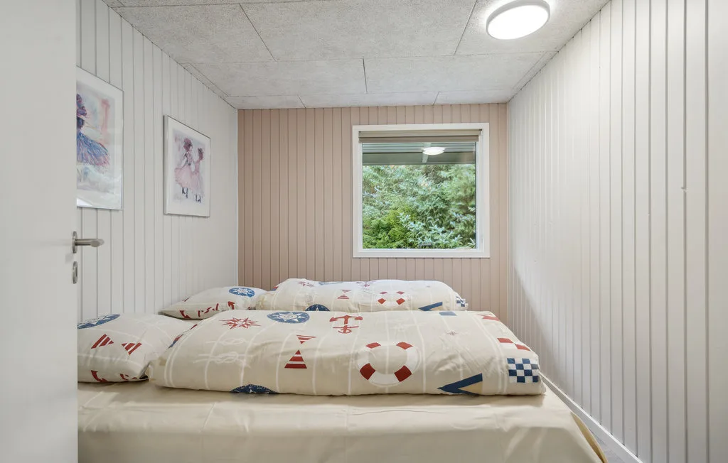 Un dormitorio con una cama baja cubierta con ropa de cama estampada y una ventana con vistas a la vegetación.