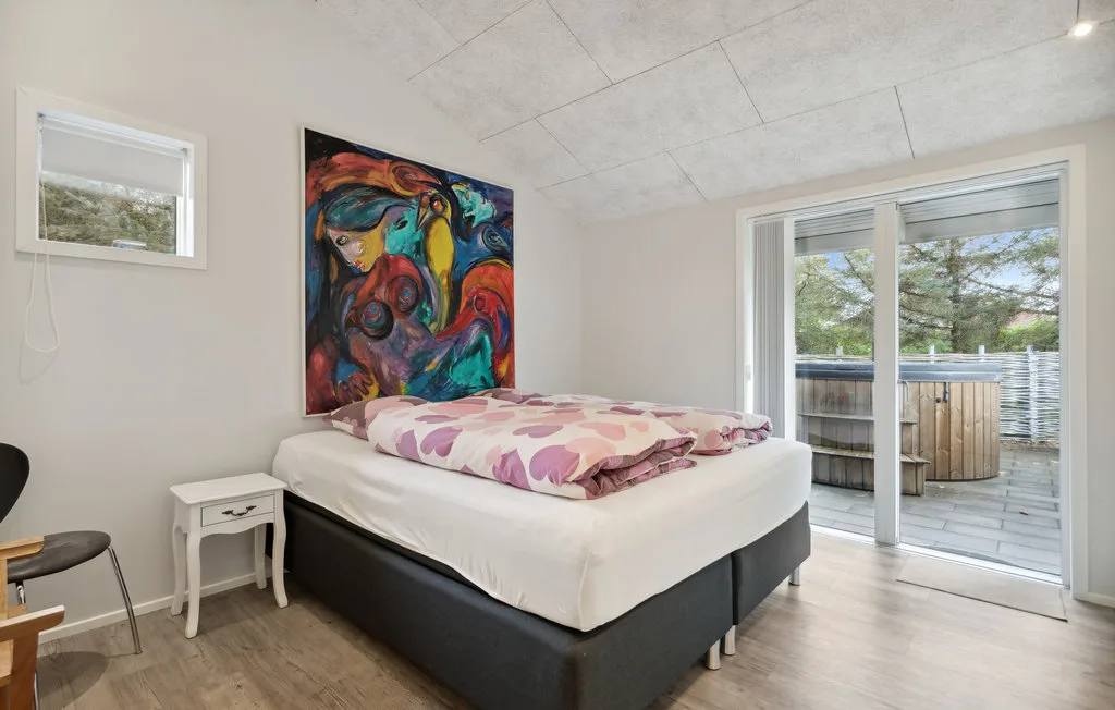 Un dormitorio con una cama, arte colorido en la pared y puertas corredizas de vidrio hacia una terraza.