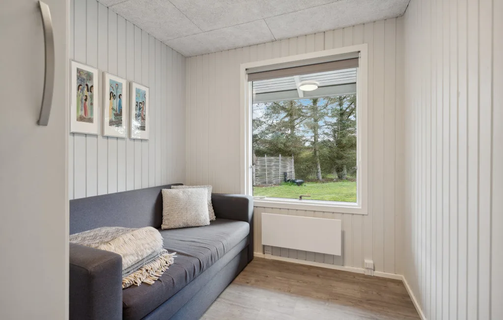 Una habitación compacta con un diván gris bajo cuadros enmarcados y una ventana grande.