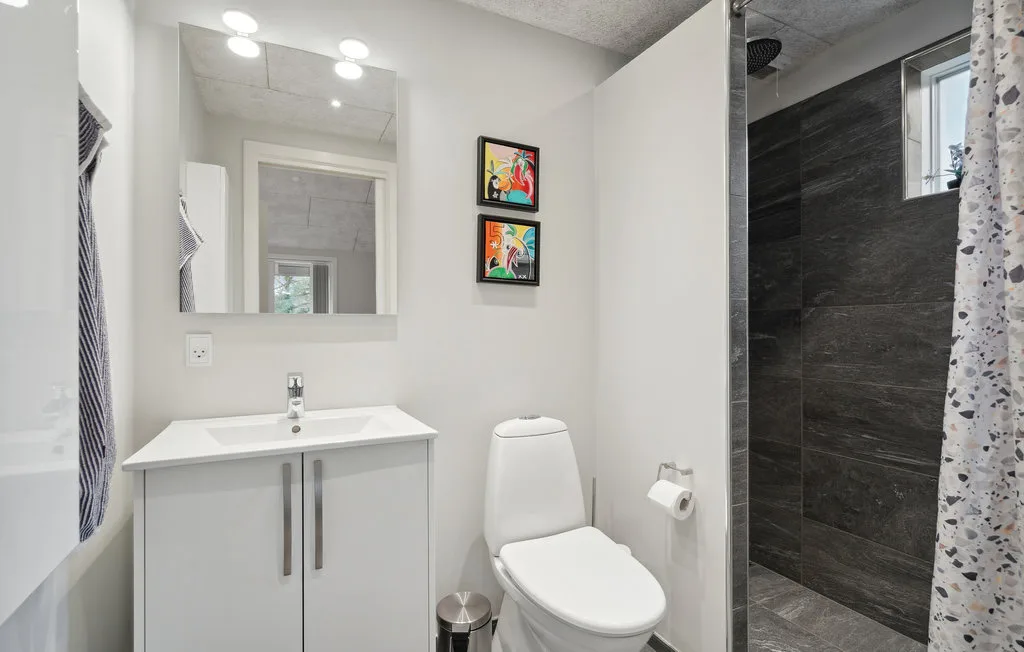 Un baño con lavabo, inodoro y ducha de azulejos oscuros.