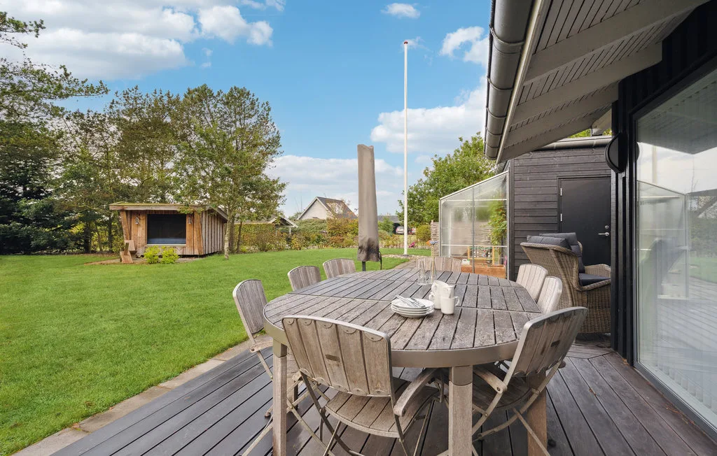 Una zona de comedor al aire libre con mesa y sillas de madera junto a un césped verde.