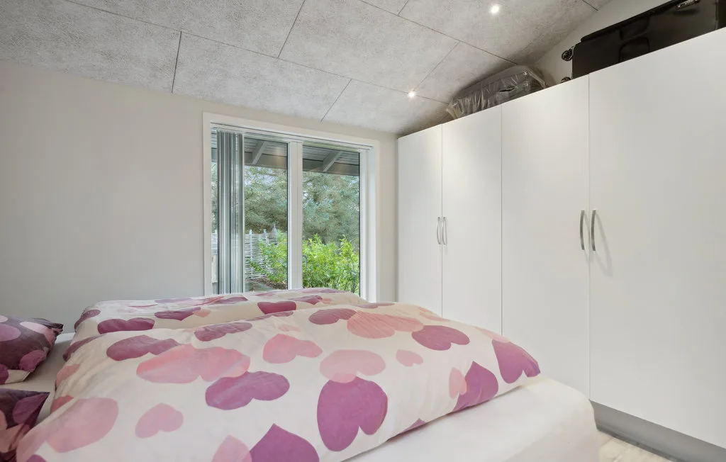 Un dormitorio con una cama cubierta con un edredón rosa de corazones junto a armarios blancos.