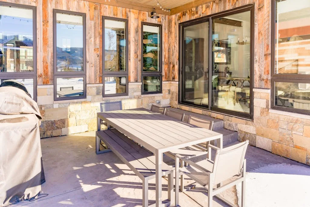 Un patio exterior con una mesa de comedor y sillas junto a grandes ventanas.