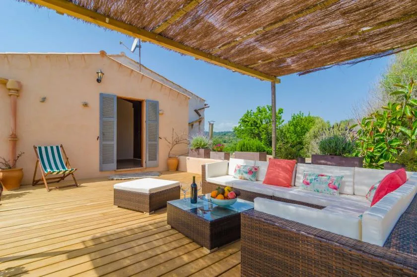 An outdoor patio has cushioned seating and a low table beneath a shaded canopy.