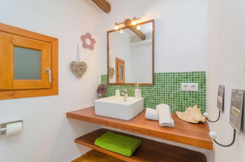 A bathroom vanity with a white sink, wood counter, and green tiled backsplash.