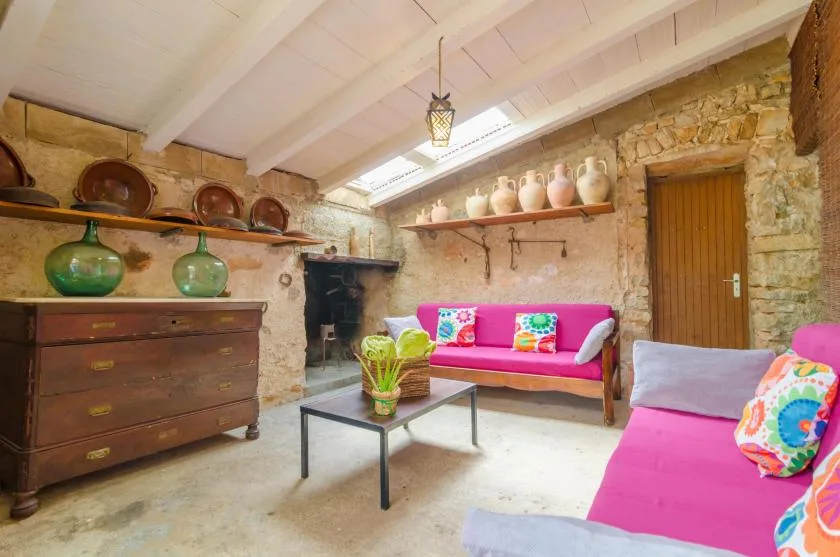 A stone-walled living room with pink seating and a wooden chest.