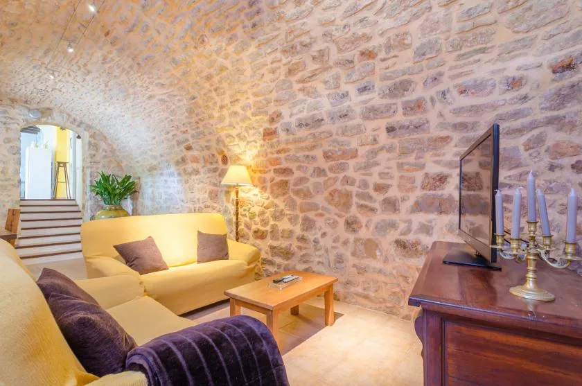 A stone-walled living room with yellow seating, a coffee table, and a television.