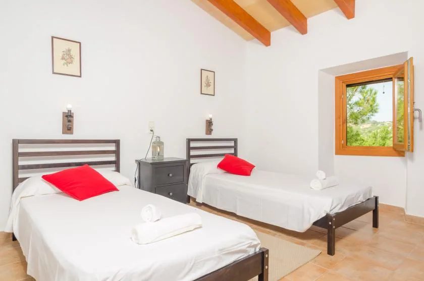 A bright bedroom with two single beds and an open window.